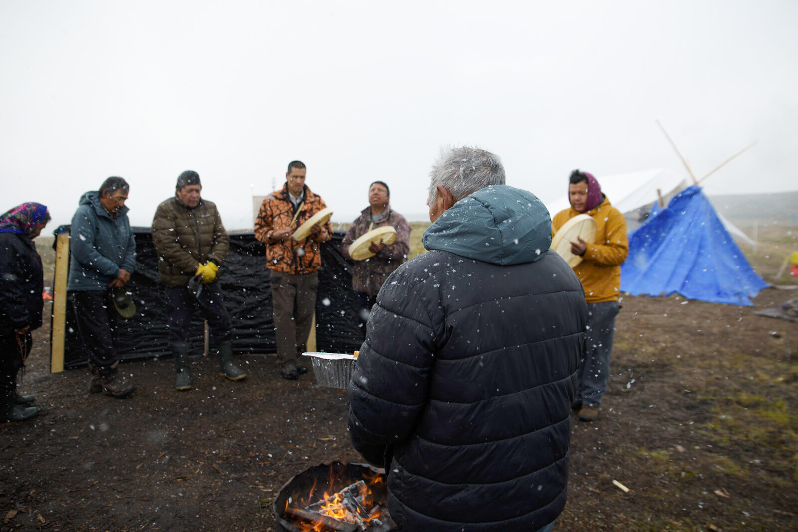 Drummers sing while Louis Zoe feeds the fire with an offering of bread and tobacco, a way to ask The Creator for safe travel and offer thanks before the day begins.